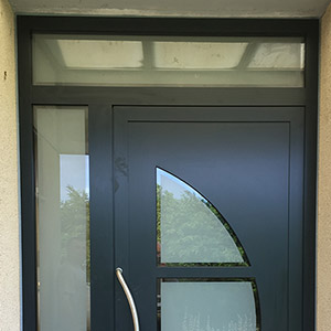 Porte d'entrée avec une imposte en verre au-dessus et une vitre sur le côté.